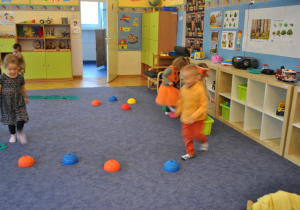 Dzieci bez bucików przechodzą po ścieżce sensorycznej zbudowanej z kłujących jeżyków i innych przyborów do ćwiczeń. Ujęcie 1